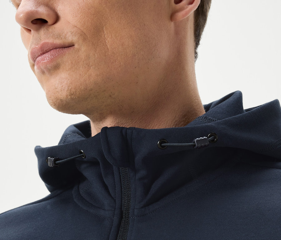 Egy férfi közeli képe, aki tengerészkék, cipzáros kapucnis pulóvert visel.