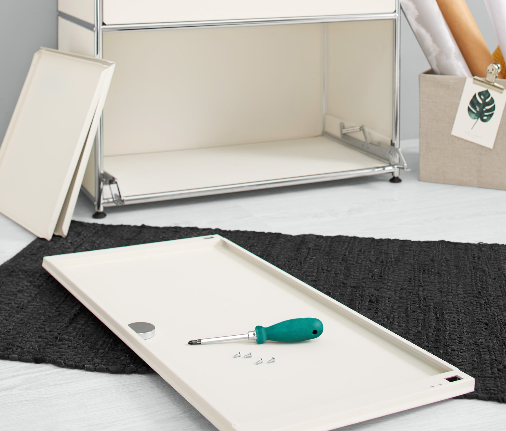 A padlón egy fehér 2 kiegészítő ajtó fém polchoz szettben, fehér, egy csavarhúzóval és csavarokkal egy komód mellett.