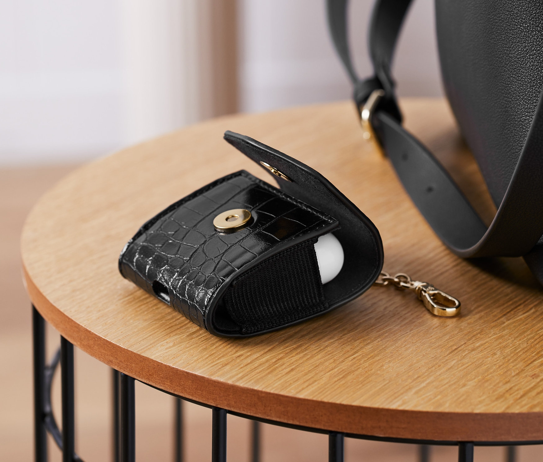 Egy fekete, krokodilbőr hatású Airpods tok nyitva fekszik egy asztalon.