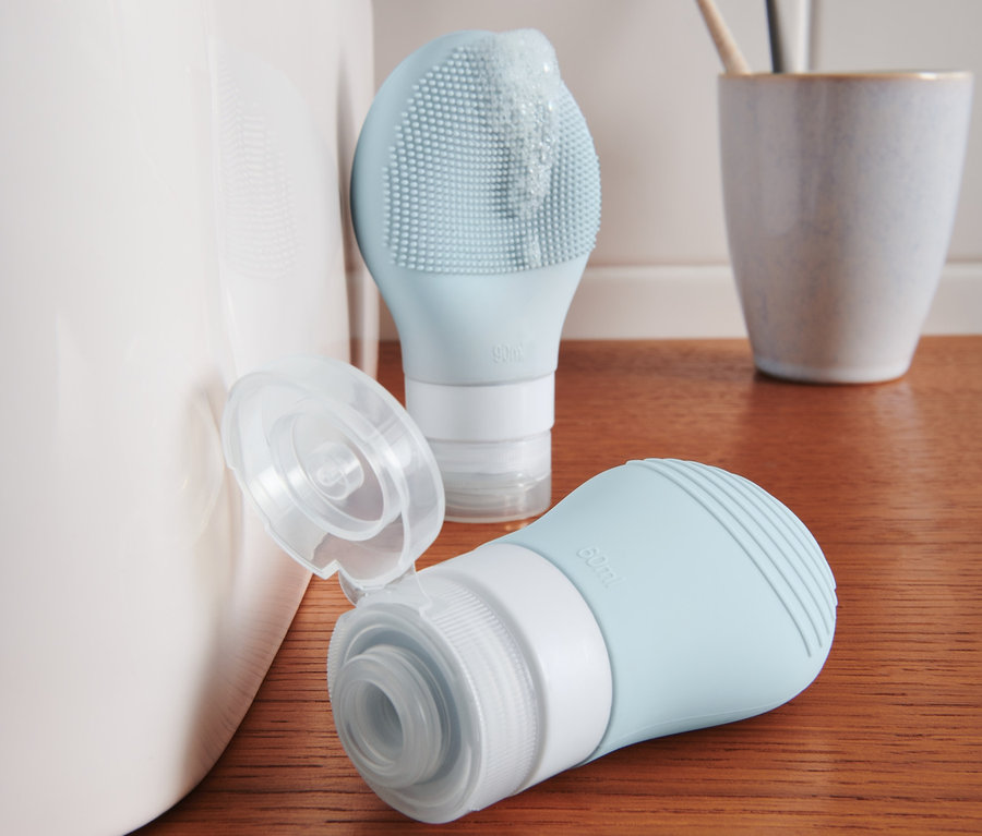 Két kék samponos flakon áll egy fa polcon egy mosdó mellett.