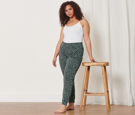 Nő trikóban és mintás szabadidőnadrágban támaszkodik egy fa székre. Rajta van a 2 női trikó is.