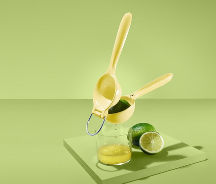 Sárga citrusprés egy pohár gyümölcslé és egy lime fölött zöld háttérrel.