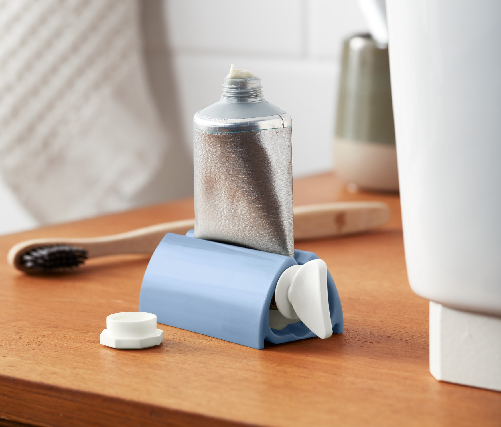 Ezüst színű tubus kék tubuskinyomóban, fa polcon.