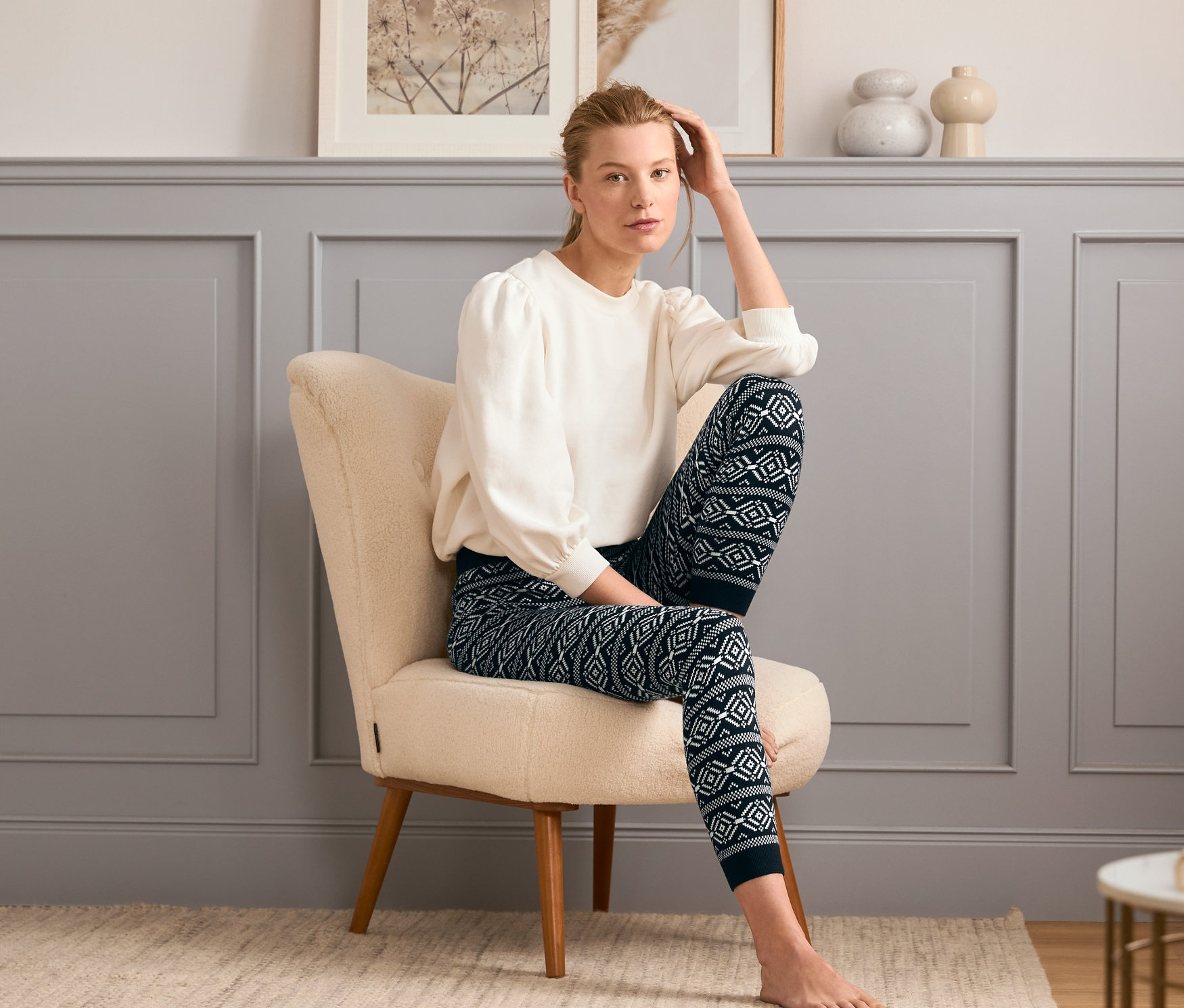 Nő ül a fotelben, és mintás, sötétkék kötött leggingset visel.