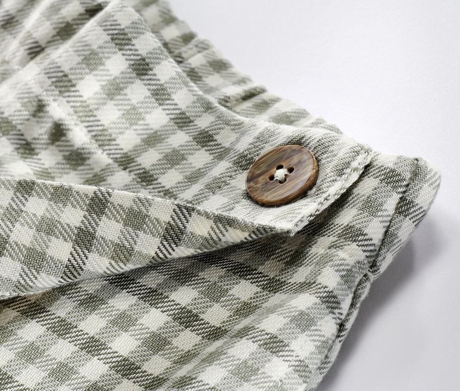 Egy kockás, zöld kislány nadrágszoknya részlete barna gombbal.