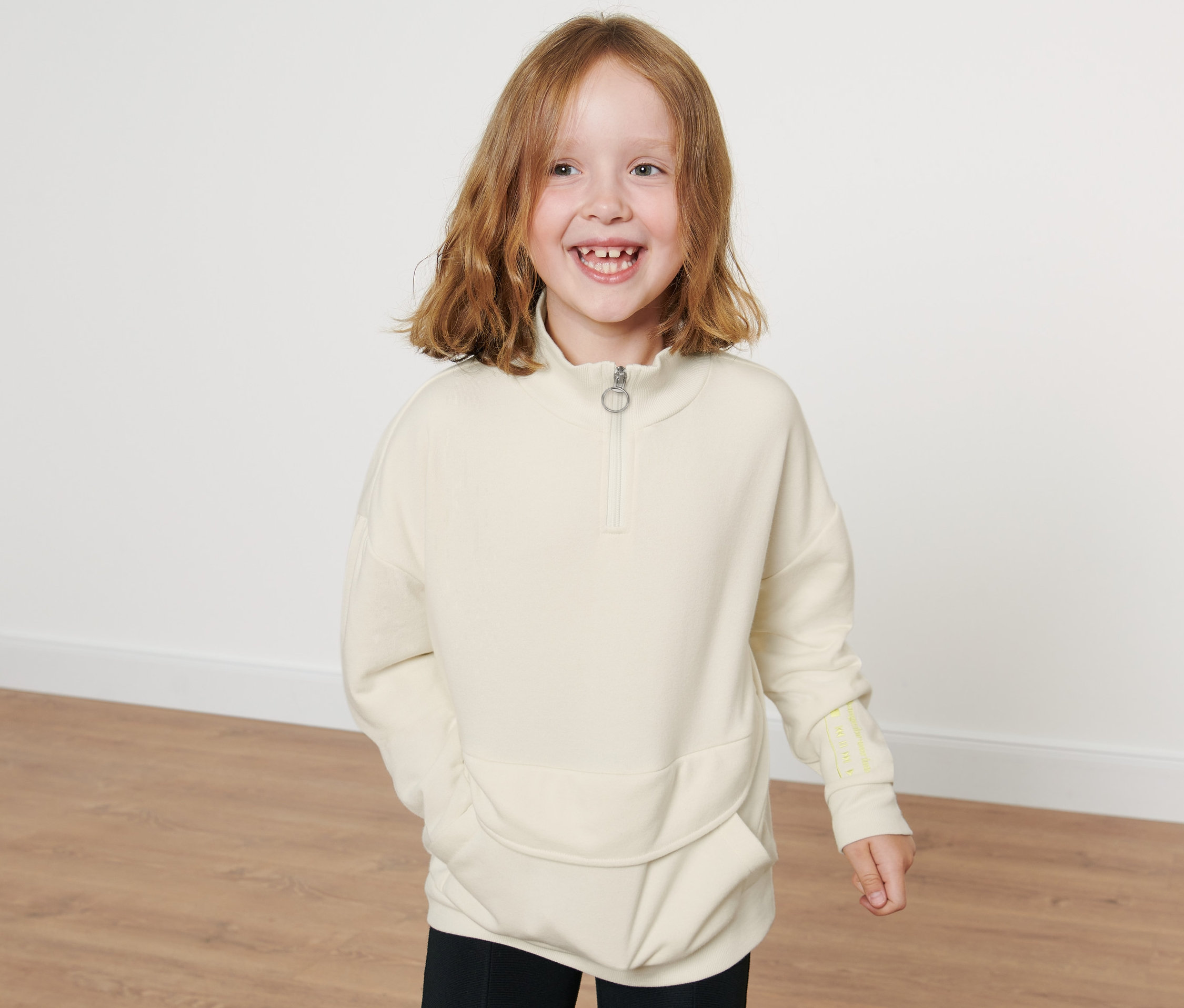 Mosolygó kislány pózol egy krémszínű, állógalléros lány pulóverben.