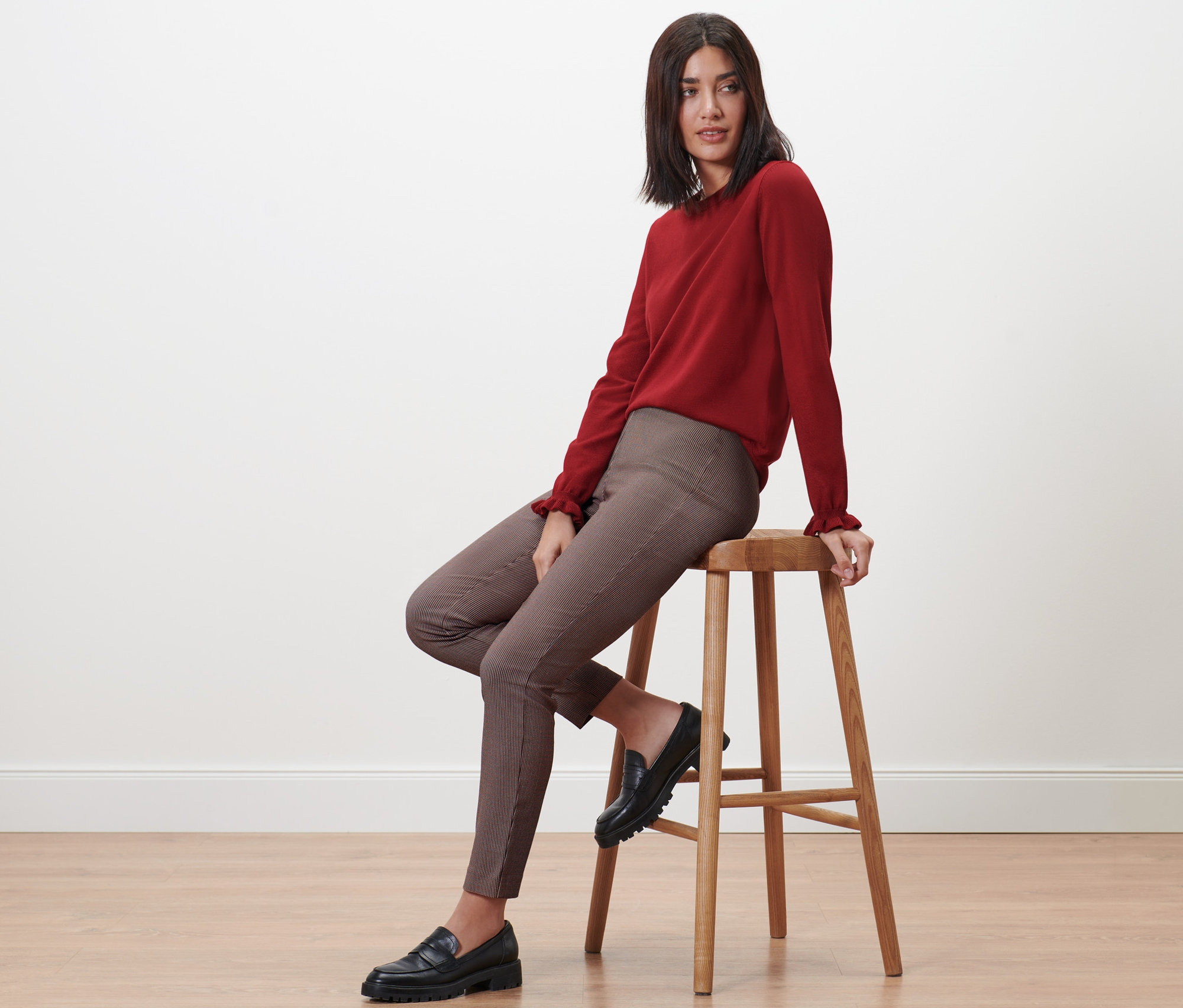 Nő ül a széken, kockás sztreccsnadrágot visel.