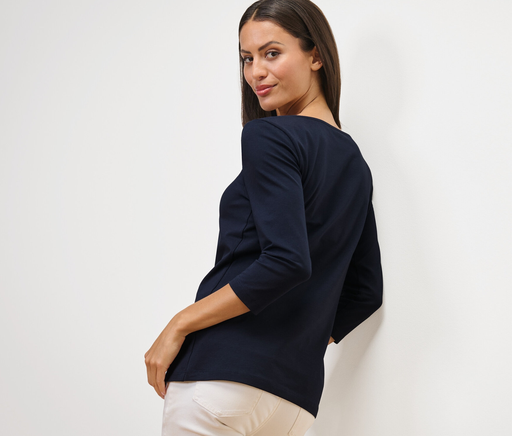 Nő néz a válla fölött, sötétkék, 3/4-es ujjú felsőt visel.