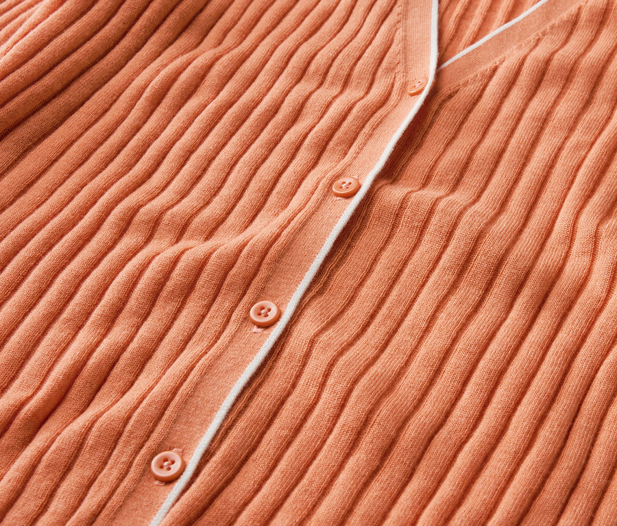 Egy barack színű, gombos, selyemmel kötött kardigán közelről.