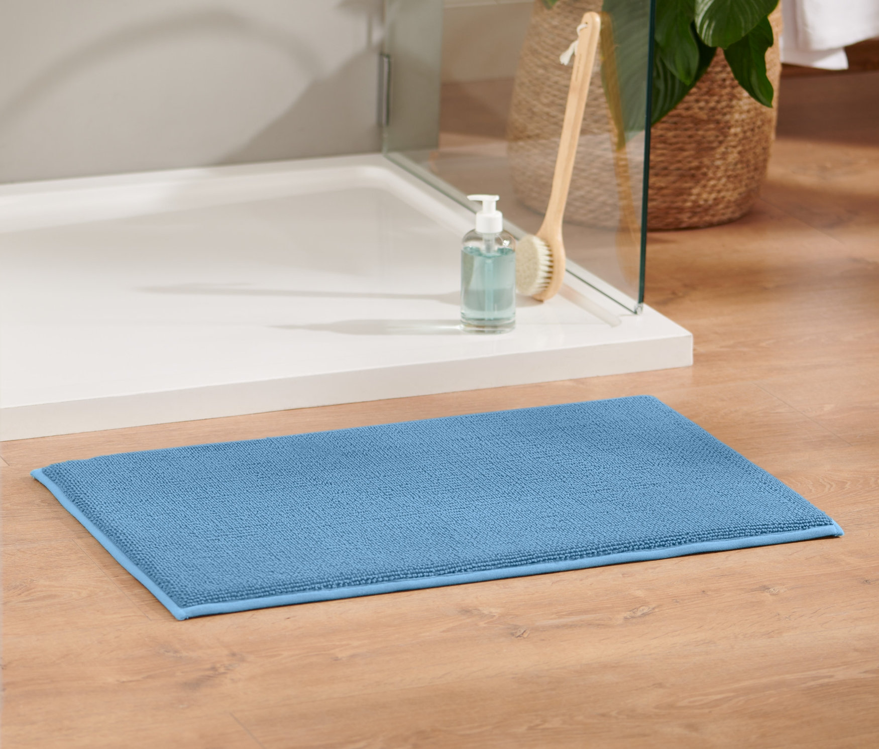 Egy kék, kb. 40 x 70 cm-es memóriahabos kádkilépő a fa padlón, a zuhanykabin mellett.