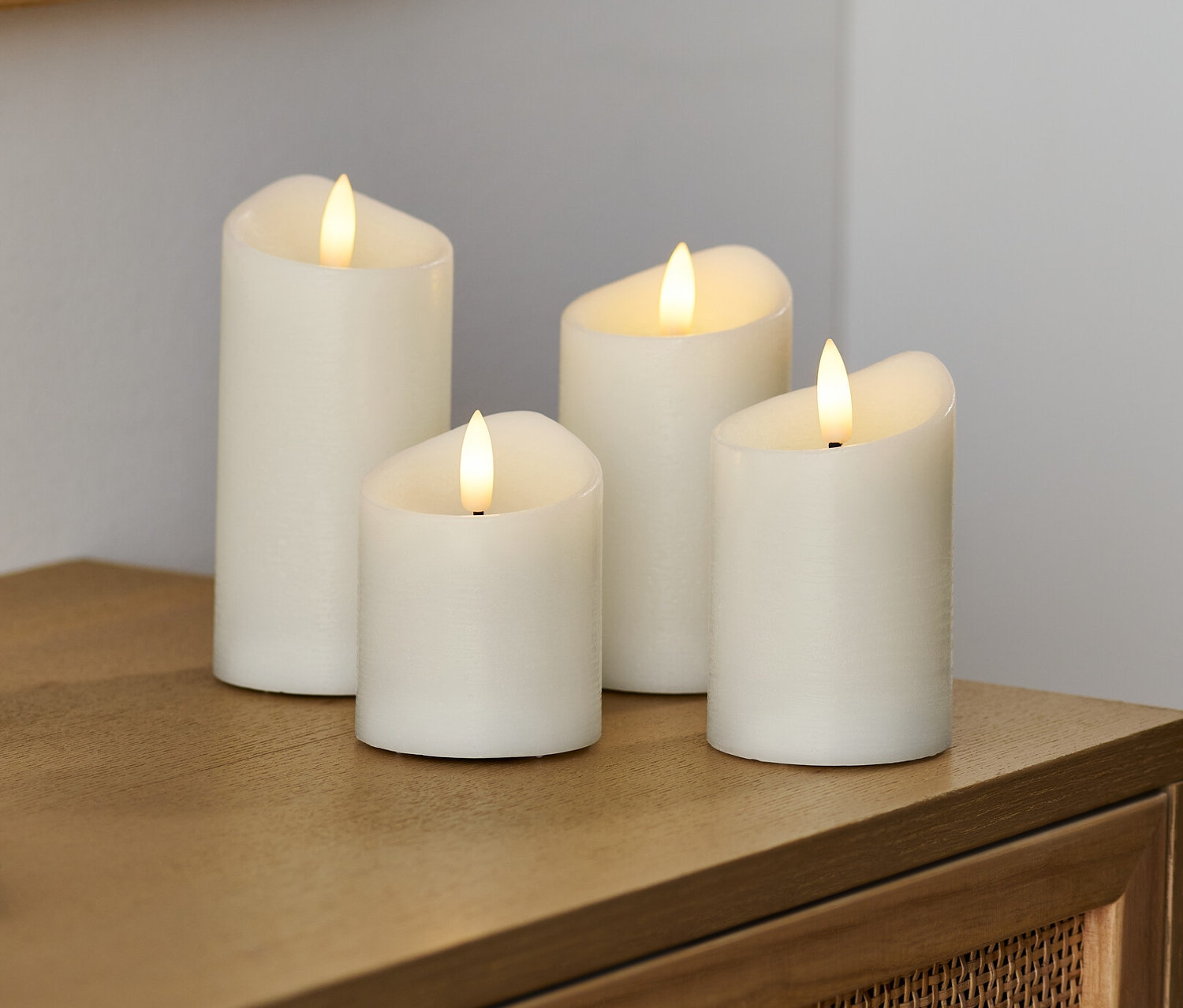 Négy krémszínű LED-es valódi viaszgyertya áll egy fa komódon.