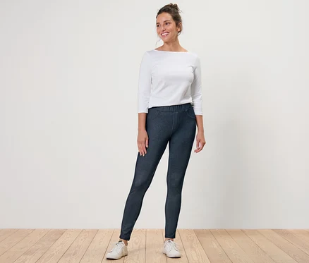 Nő farmer hatású leggingsben és fehér felsőben pózol.