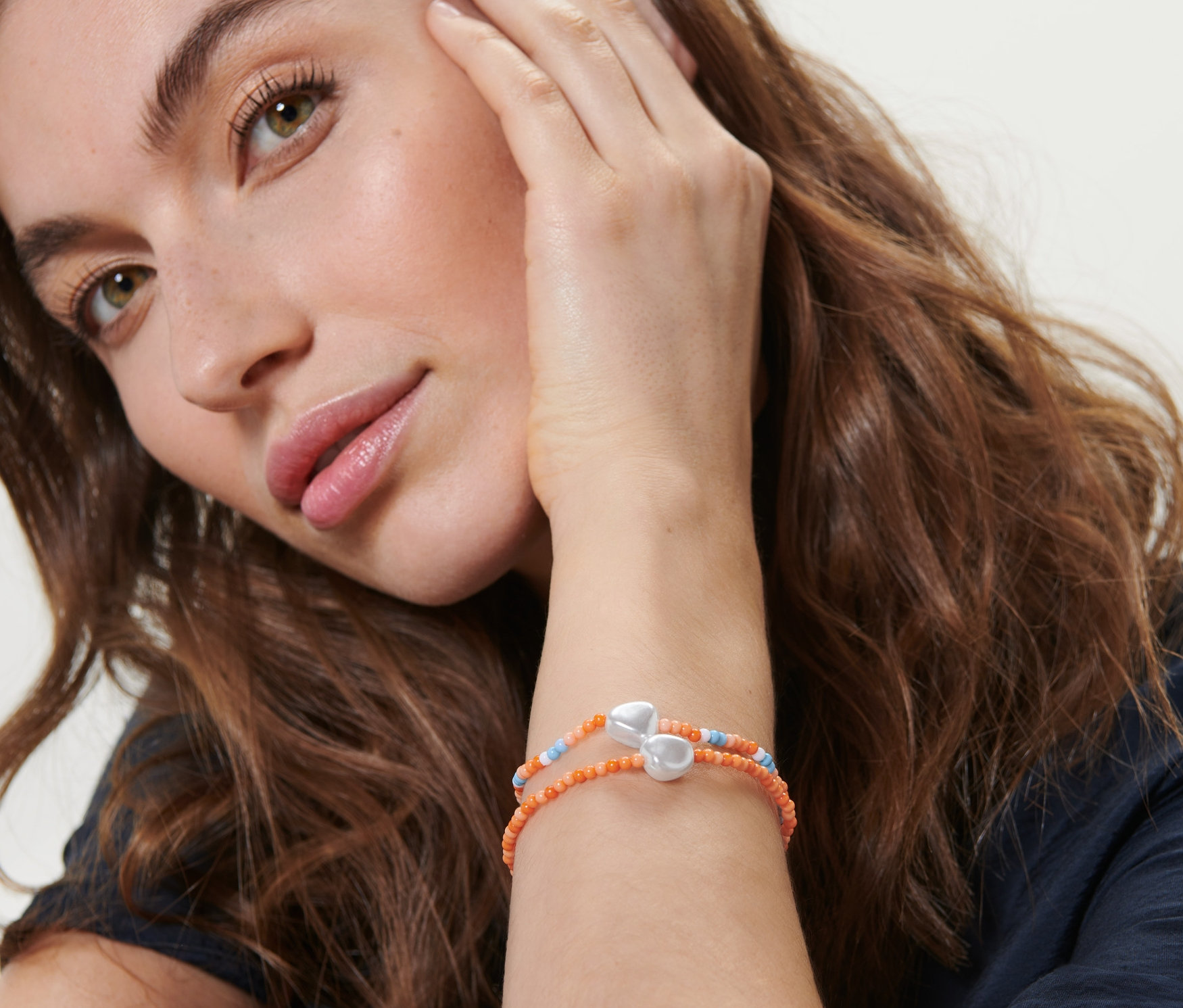 Egy nő megérinti az arcát, és 2 gyöngy karkötőt visel a csuklóján.