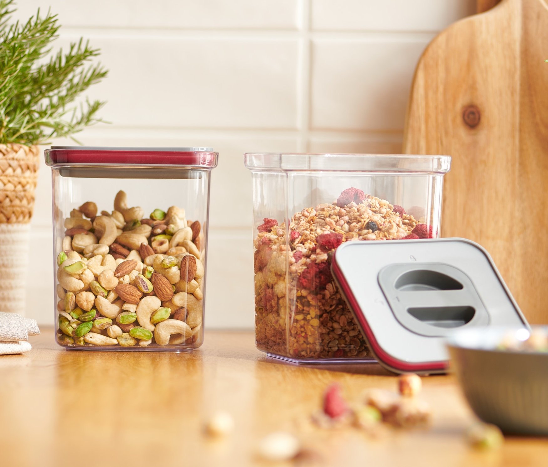 Két vákuumos frissentartó doboz áll egy fa deszkán, az egyikben dió, a másikban müzli van.