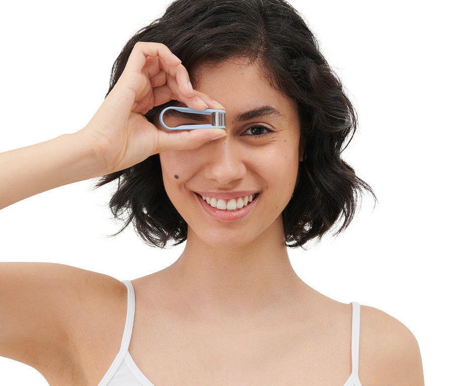 Egy nő mosolyog, és egy mini, kézi arcepilátort tart a szeme elé.