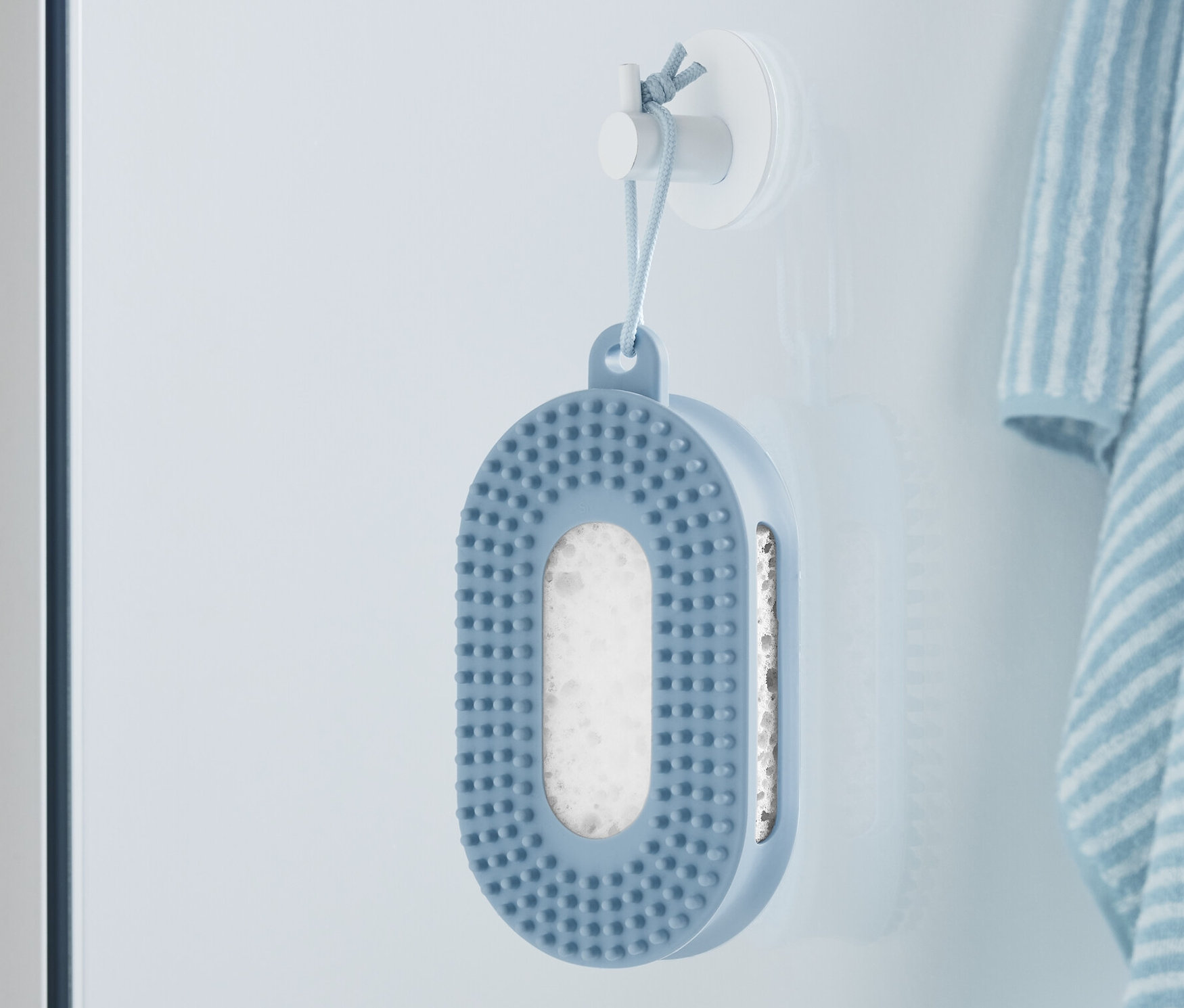 Kék mosdószivacs lóg a falon egy csíkos törölköző mellett.