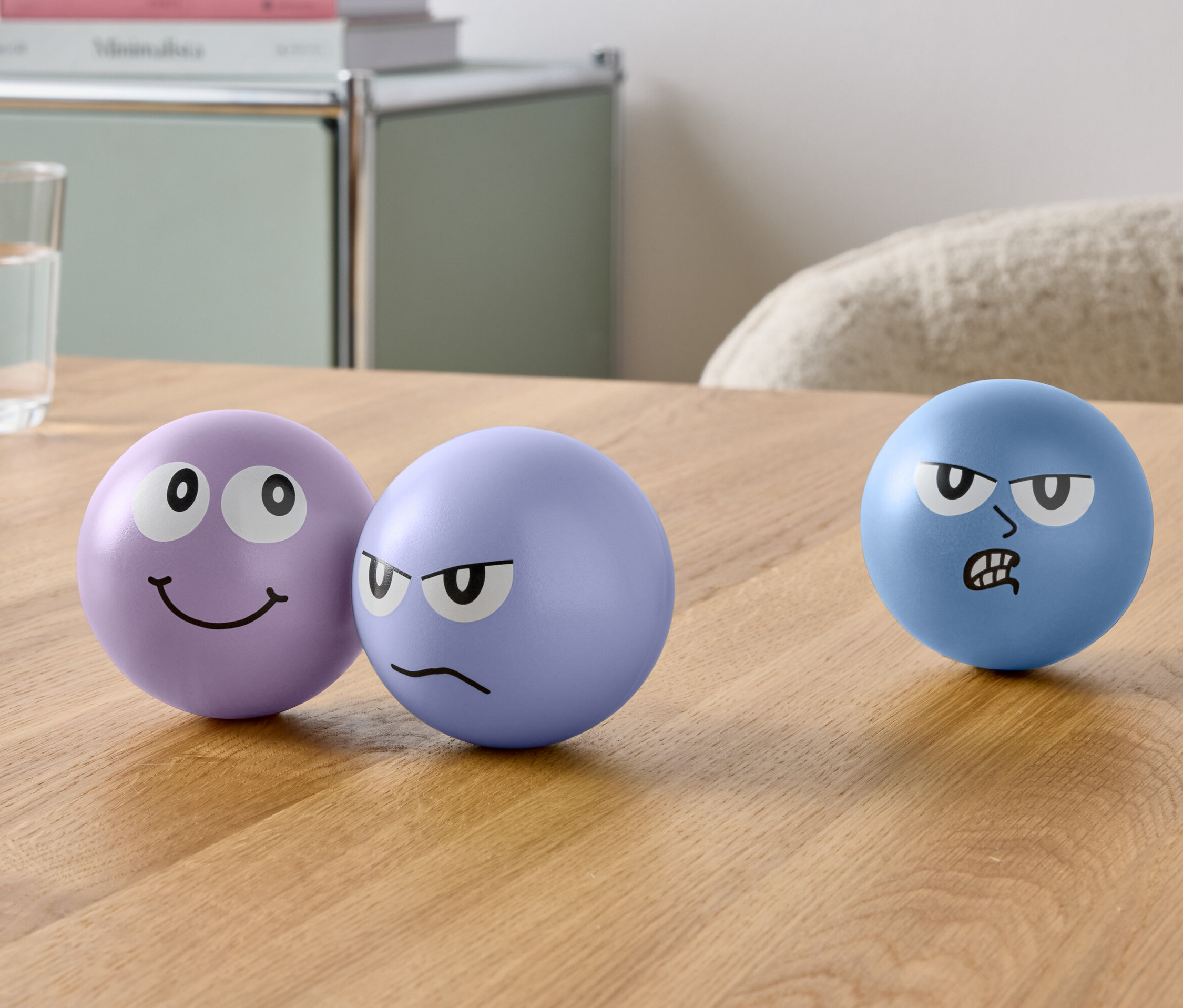 Három arccal ellátott labda és egy pohár víz van az asztalon.