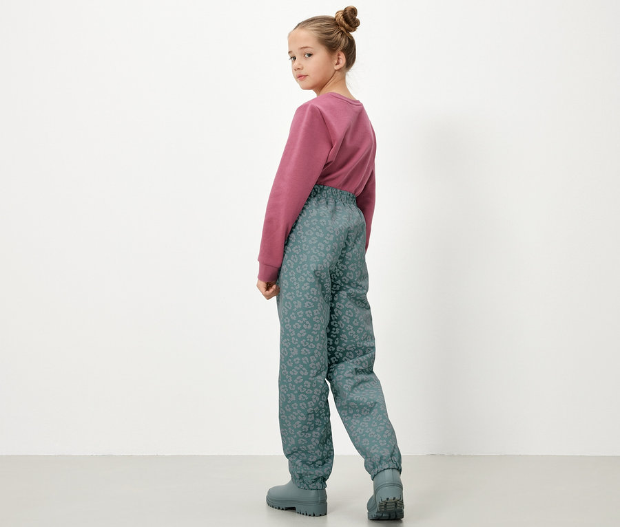 Hátulról látható pulóvert és fényvisszaverő elemekkel ellátott gyermek esőnadrágot viselő lány.