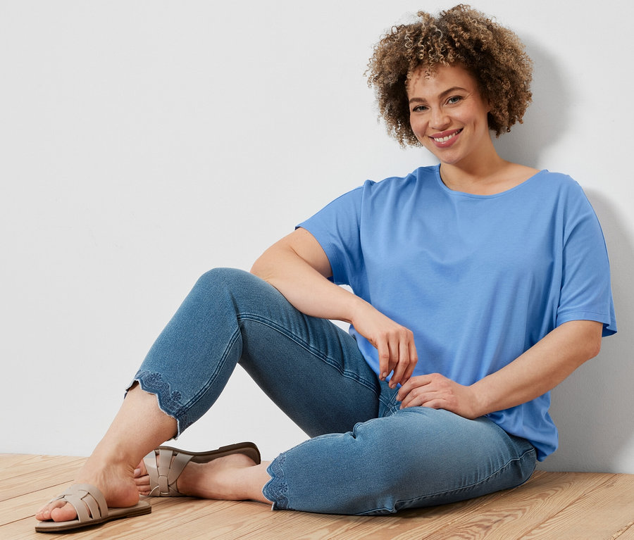 Nő ül a fapadlón, világoskék női pólóblúzt és 7/8-os, lyukhímzéses tregginget visel.
