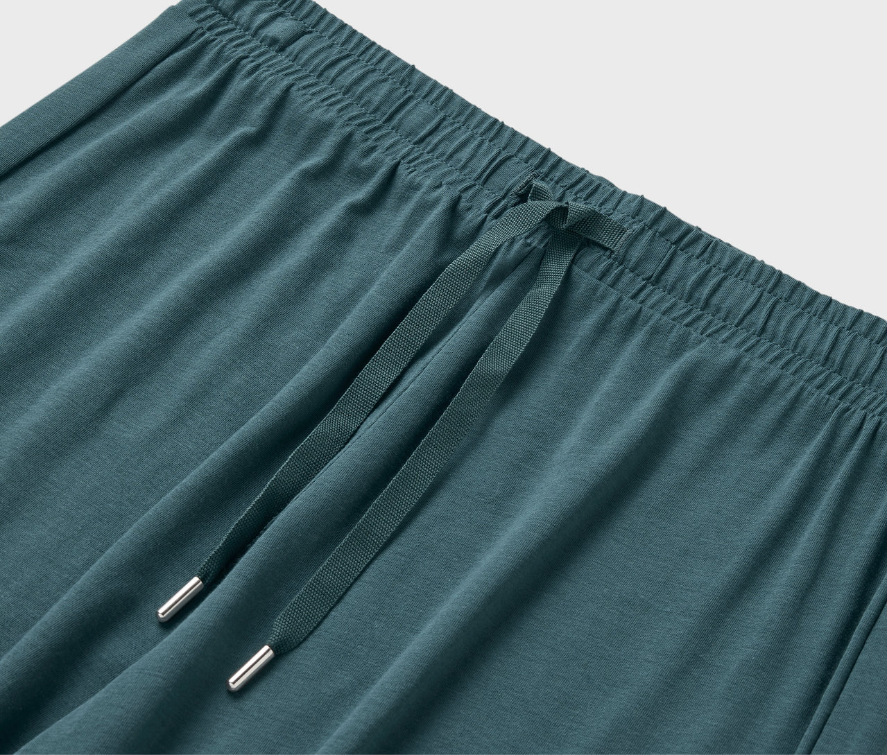 Közelkép egy kékeszöld színű melegítőnadrág rugalmas derékrészéről és húzózsinórjáról.