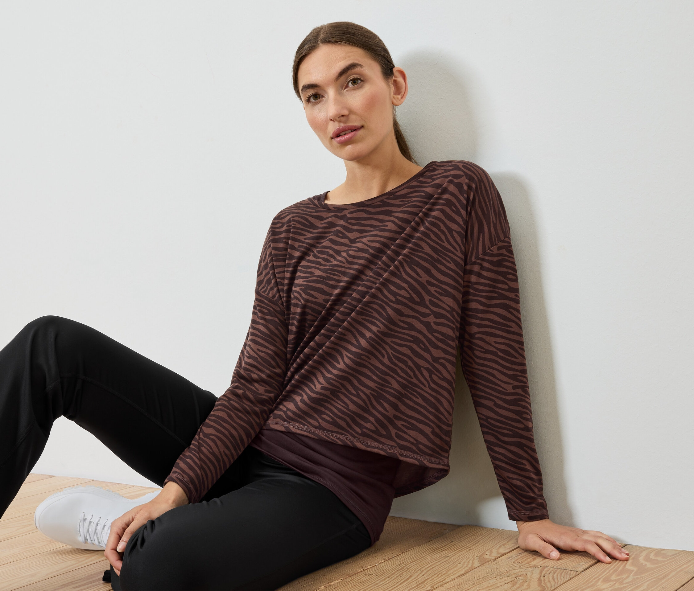 Nő ül a padlón barna-fekete zebracsíkos felsőben és fekete nadrágban.