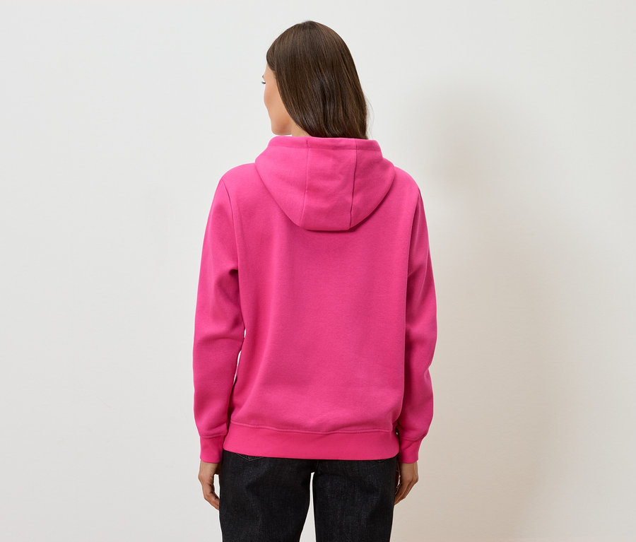 Hátulnézet egy barna hajú nőről rózsaszín kapucnis pulóverben és fekete nadrágban.