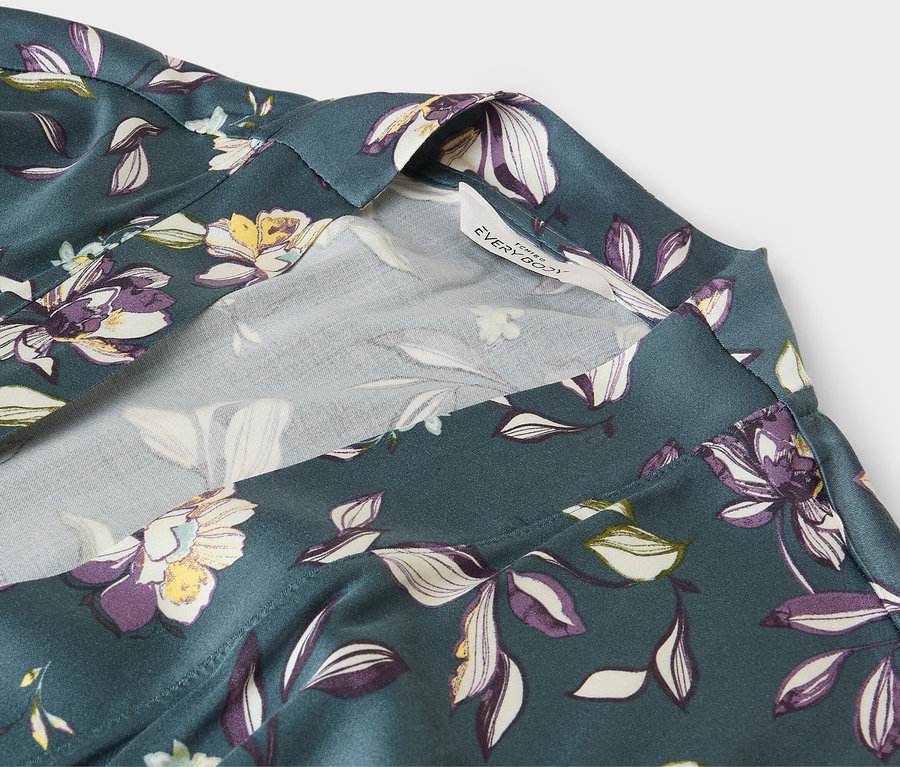 Egy zöld, virágmintás köntös részlete fehér szegéllyel.