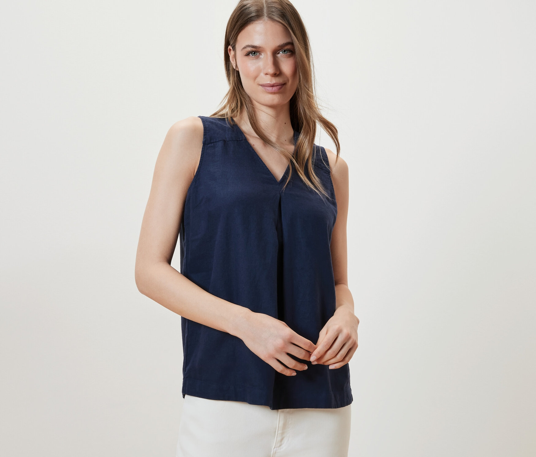 Nő pózol sötétkék, lenvászon ujjatlan blúzban.