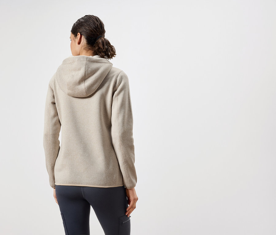 Hátulról látható egy nő bézs kapucnis pulóverben és sötétkék nadrágban.