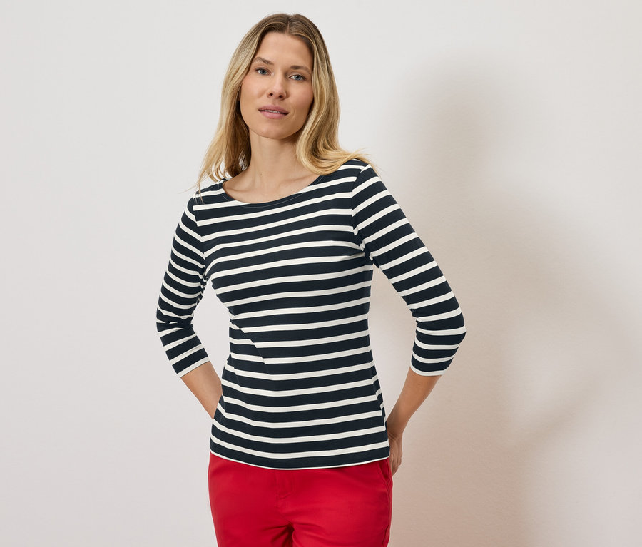 Szőke nő visel egy csíkos, háromnegyedes ujjú felsőt és piros nadrágot.