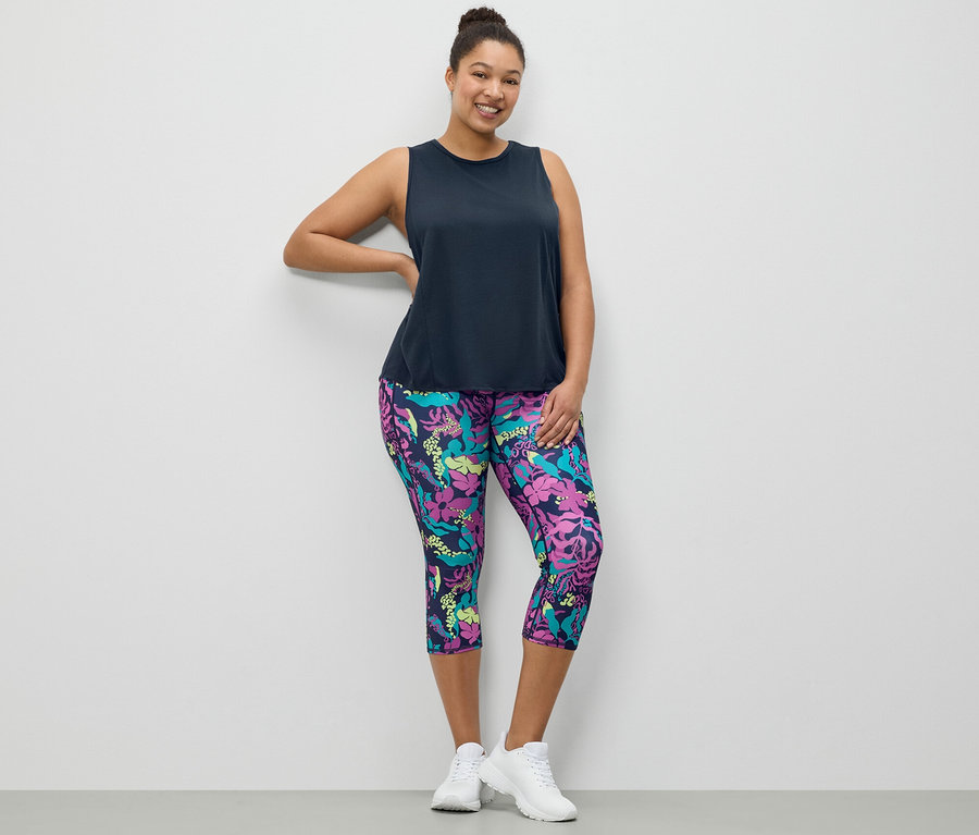 Egy nő pózol sötétkék sporttopban és egy mintás 3/4-es sportnadrágban.