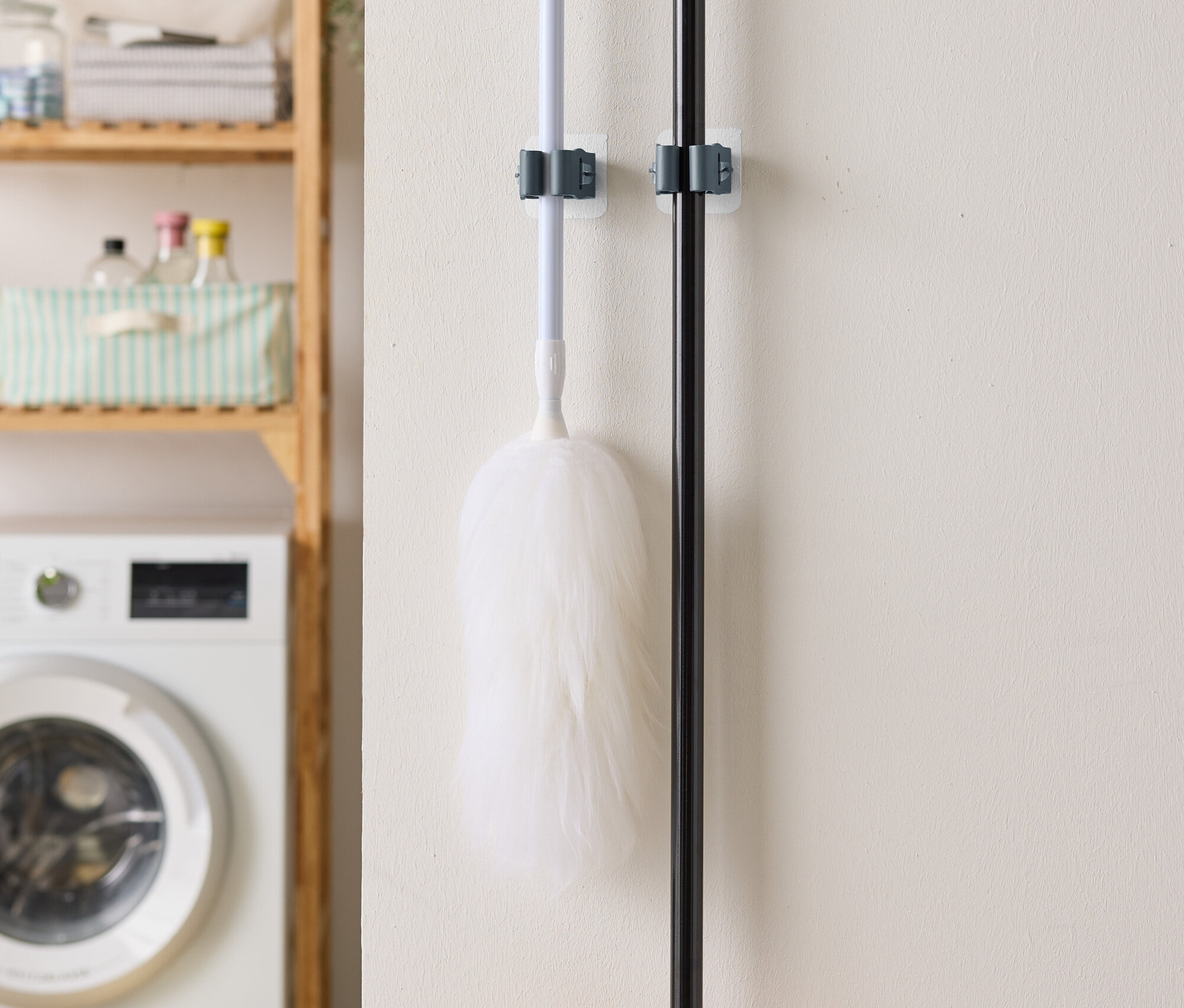 Egy portörlő és egy seprű lóg a falon, a háttérben egy mosógép és egy polc.