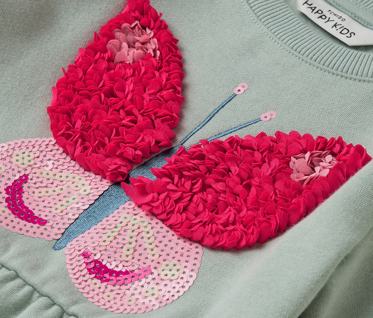 Világoszöld ruha pillangó applikációval, rózsaszín flitterekkel és piros virágokkal.