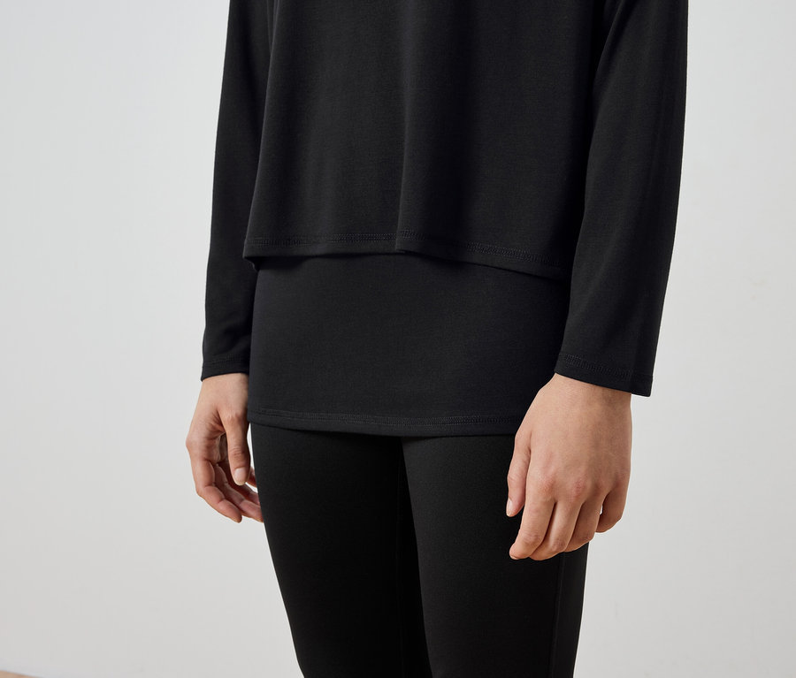 Egy személy törzse fekete hosszú ujjú inget és fekete leggingset visel.