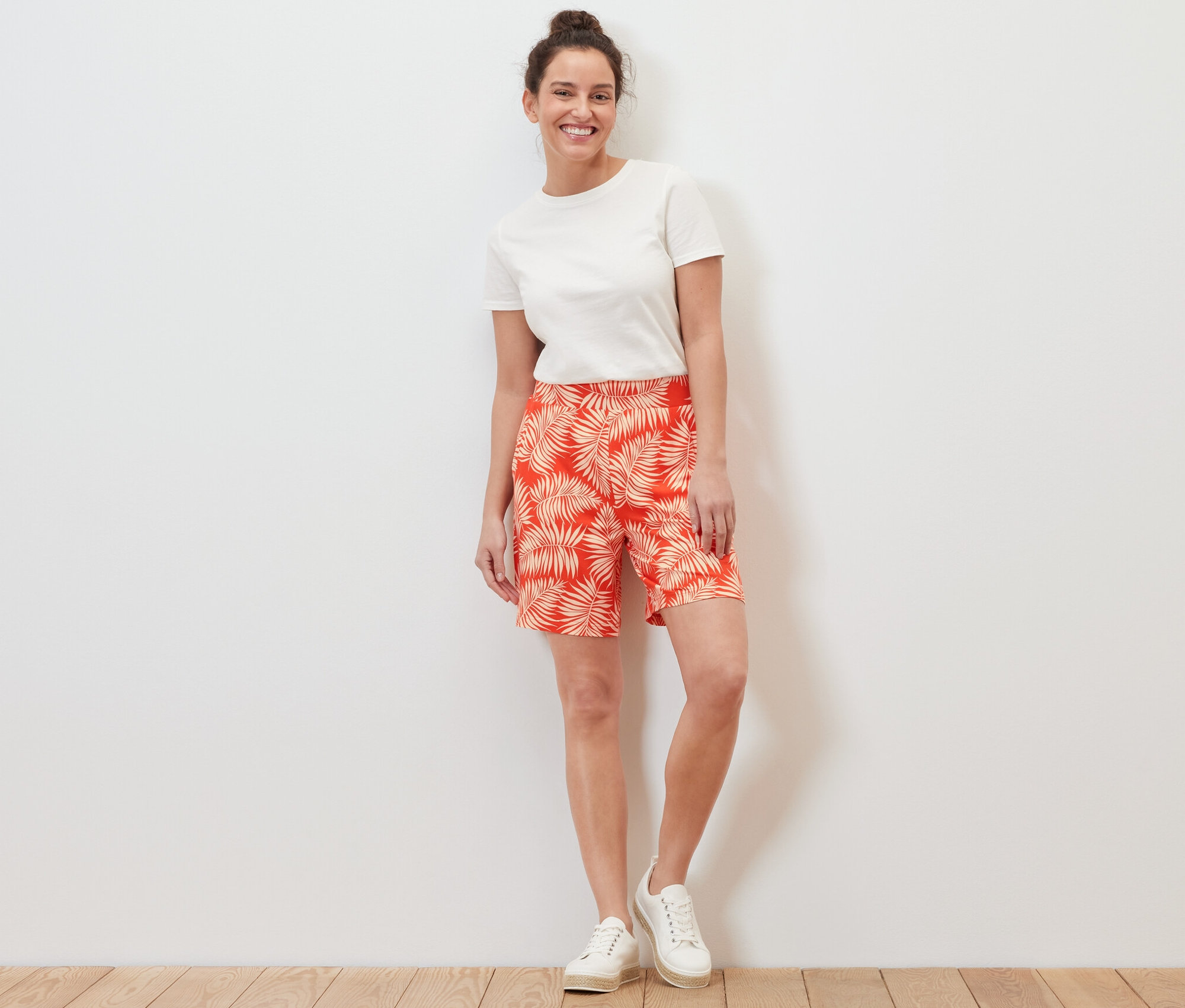 Egy nő áll, nyomott mintás jersey rövidnadrágot és fehér pólót visel.