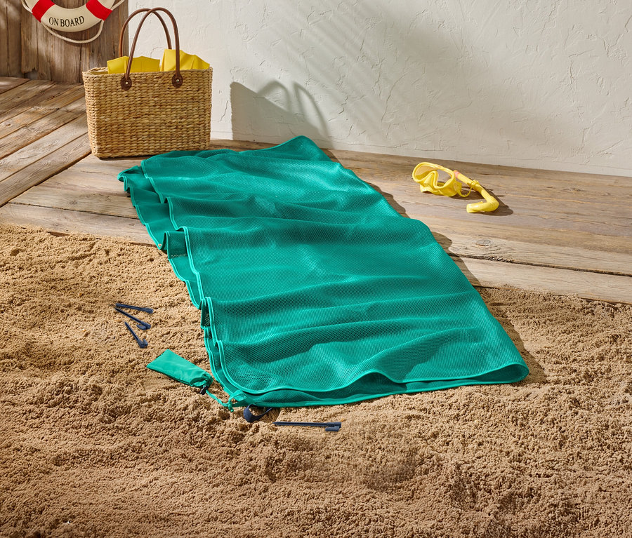 Zöld strandtörölköző homokon, mellette sárga búvárszemüveg és egy kosár.