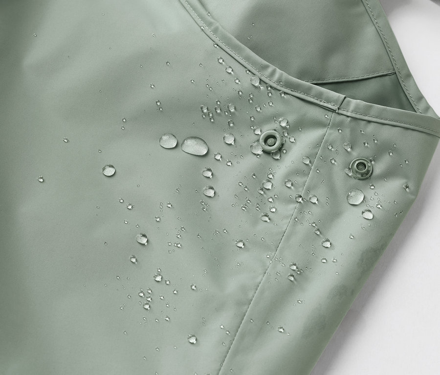 Vízálló, világoszöld anyag közelképe vízcseppekkel és két patenttal.