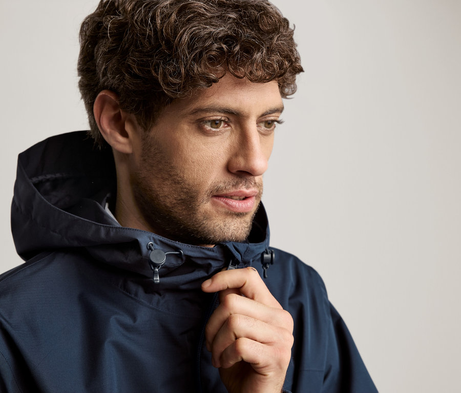 Göndör hajú férfi tengerészkék kapucnis kabátban.