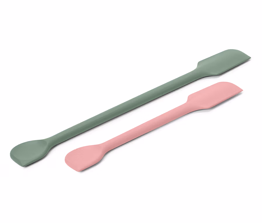 Egy zöld és egy rózsaszín spatula átlósan fekszik egy fehér háttéren.