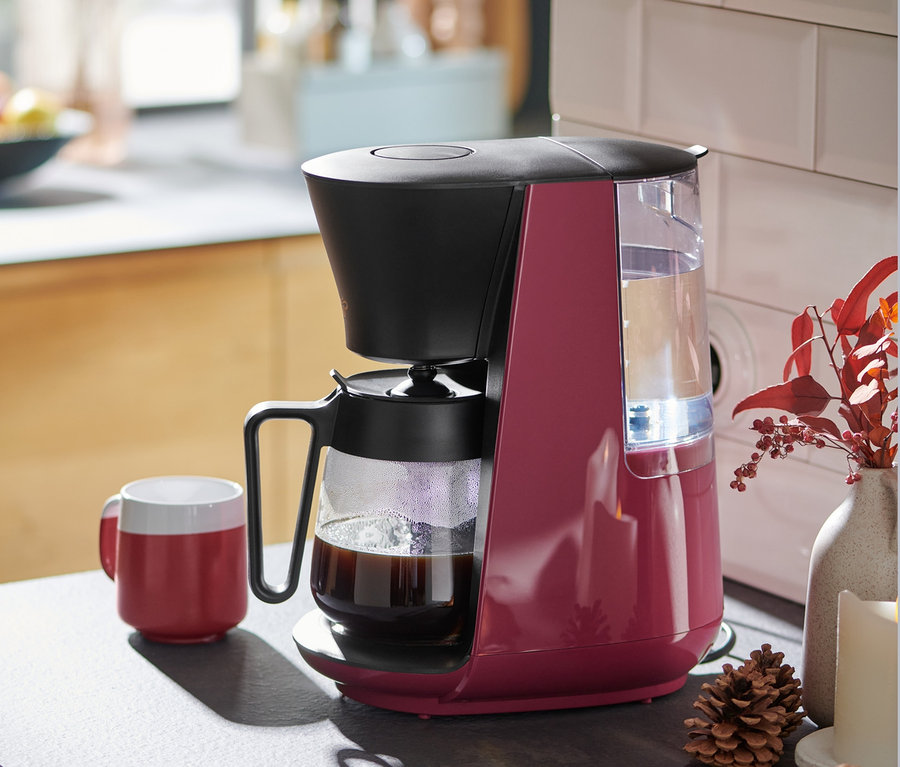 A berry színű »Let's Brew« filteres kávéfőző egy piros kávésbögre mellett áll a konyhapulton.