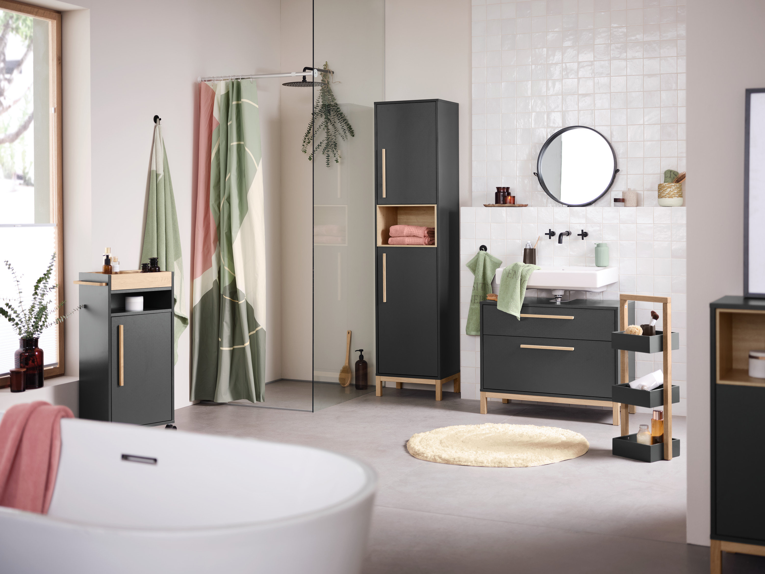 Fürdőszoba belső tér mosdóval, tükörrel és antracit Eklund fürdőszobai szekrényekkel. Előtérben egy fürdőkád.