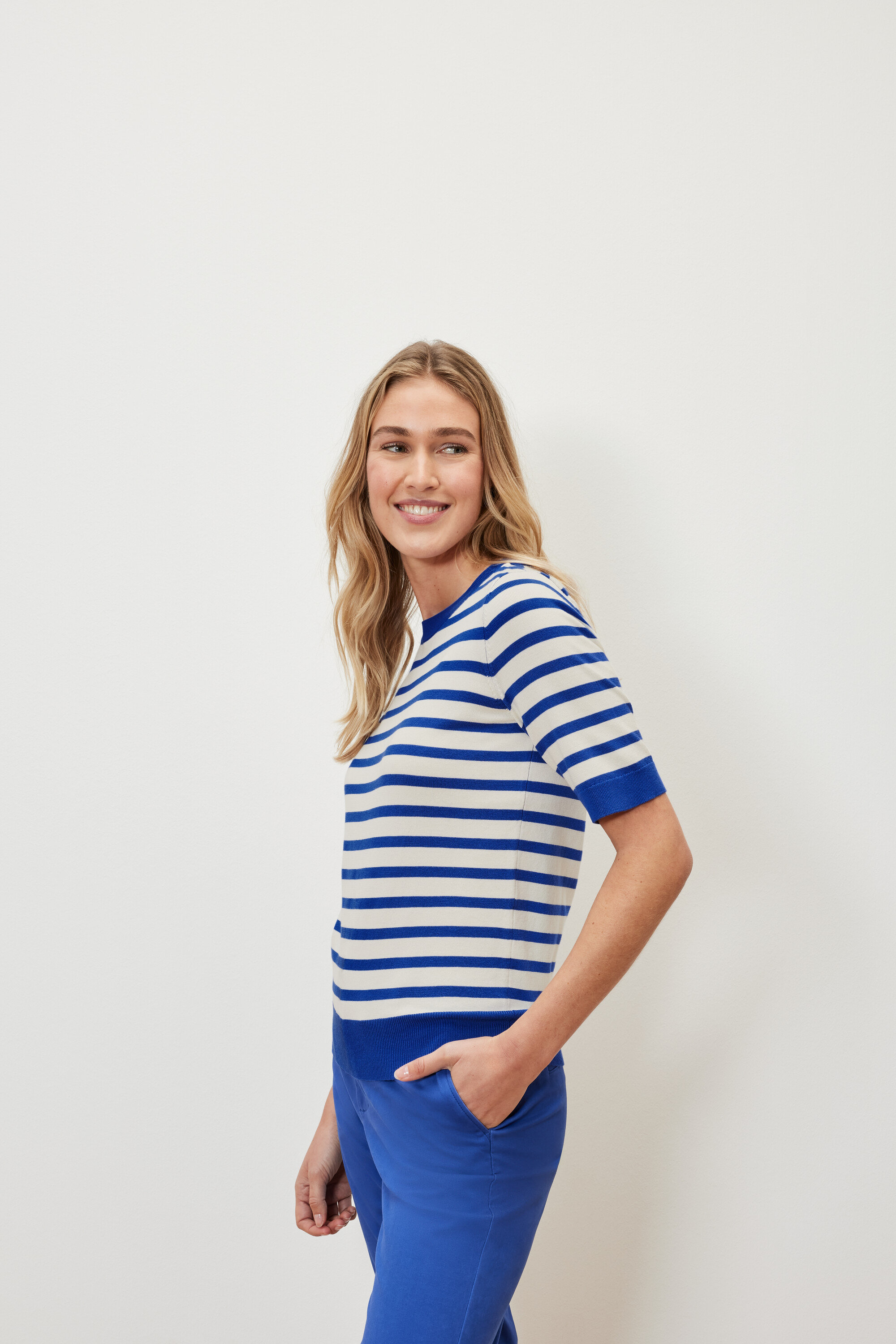 Nő visel egy csíkos, vékony kötött pulóvert és kék nadrágot.