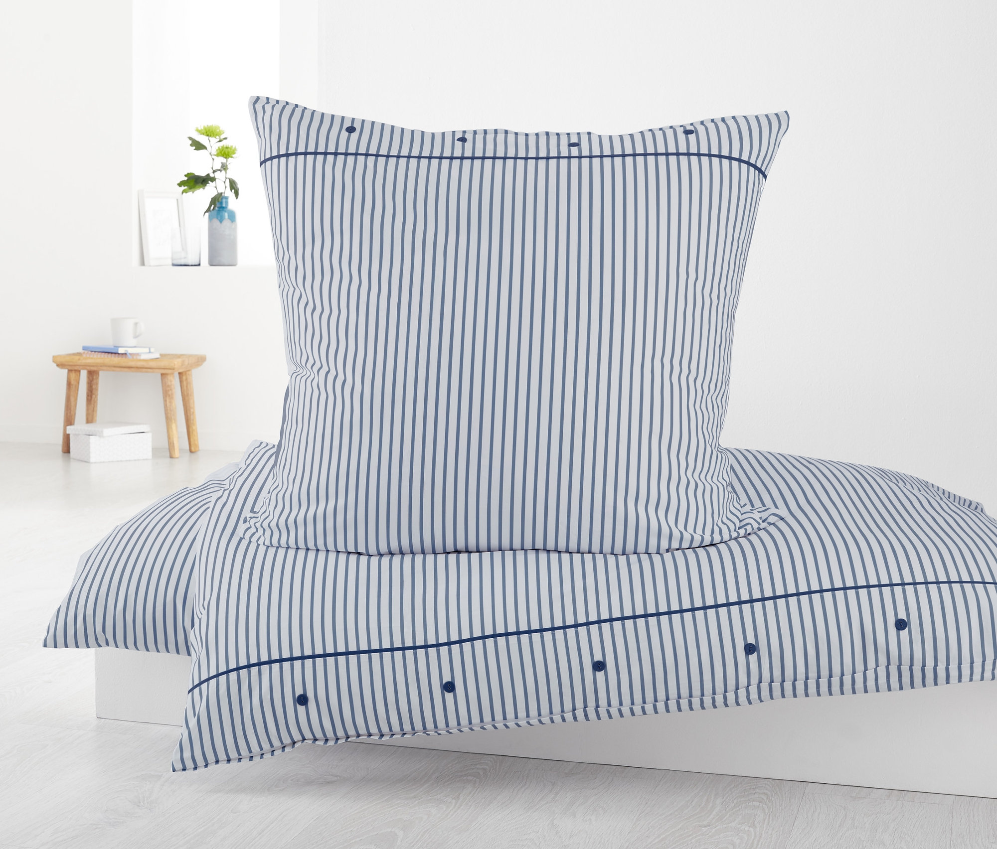 Csíkos perkál ágynemű, kétszemélyes méretben, párnával egy fehér ágyon.