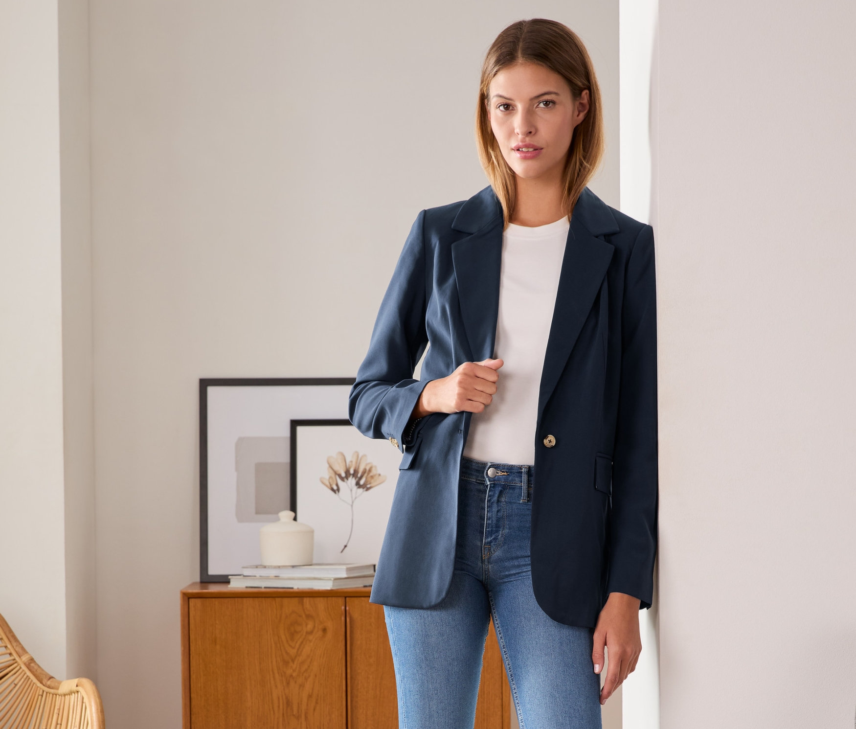 Nő pózol szövött blézerben, farmerban és tornacipőben.