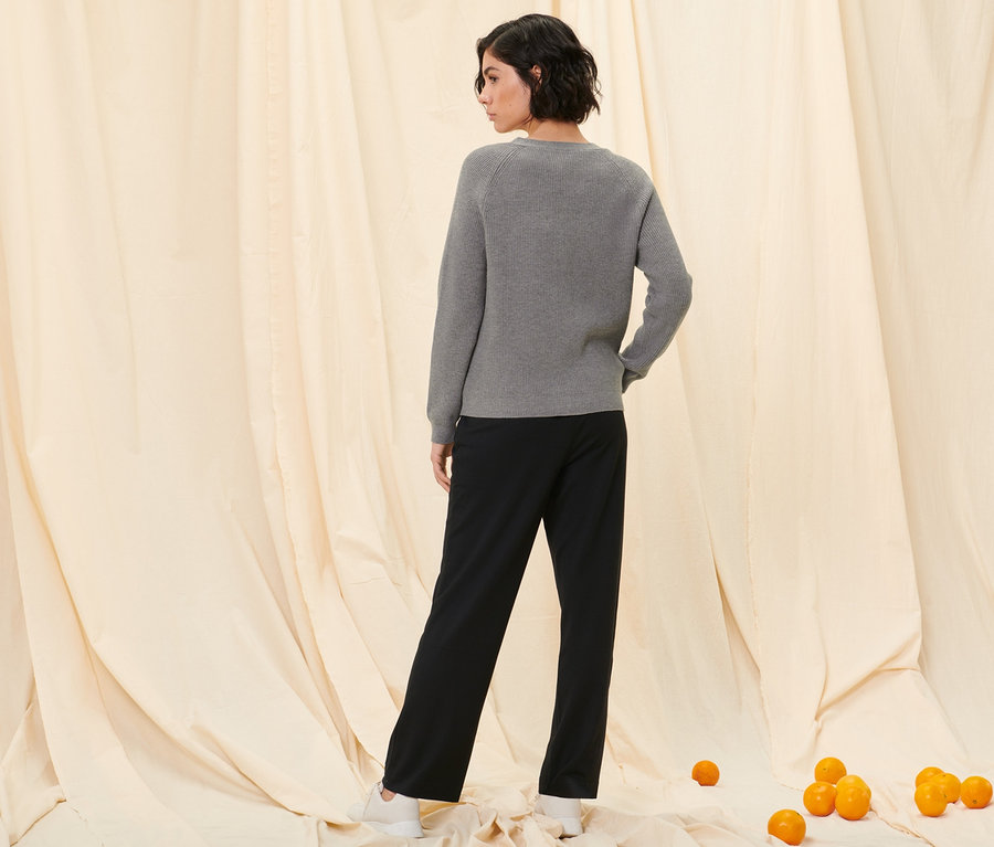 Egy nő háttal áll a kamerának, és kötött kardigánt és fekete szabadidőnadrágot visel.