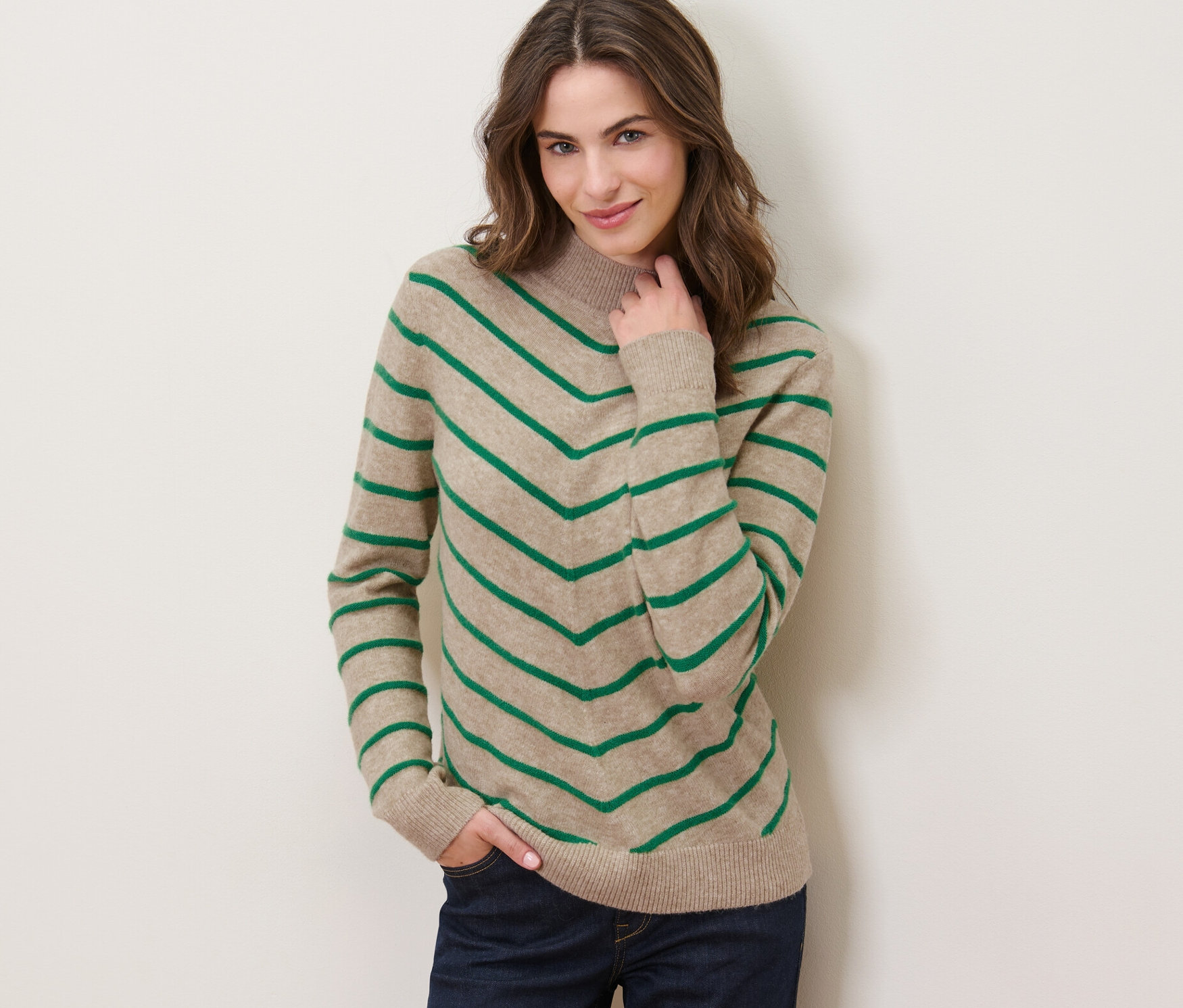 Nő pózol krémszínű, csíkos kötött pulóverben, állógallérral.