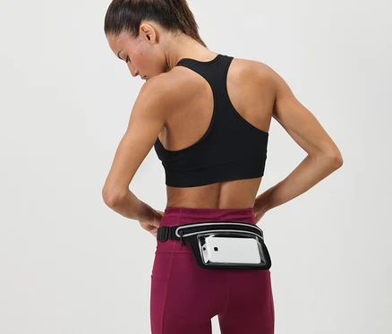 Nő igazítja az Okostelefon tartó sportövet a dereka körül. Sportmelltartót és leggingset visel.