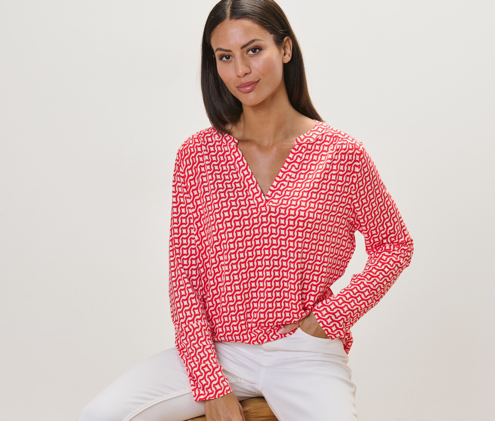 Nő ül egy széken, piros, mintás, hosszú ujjú pólóblúz van rajta.