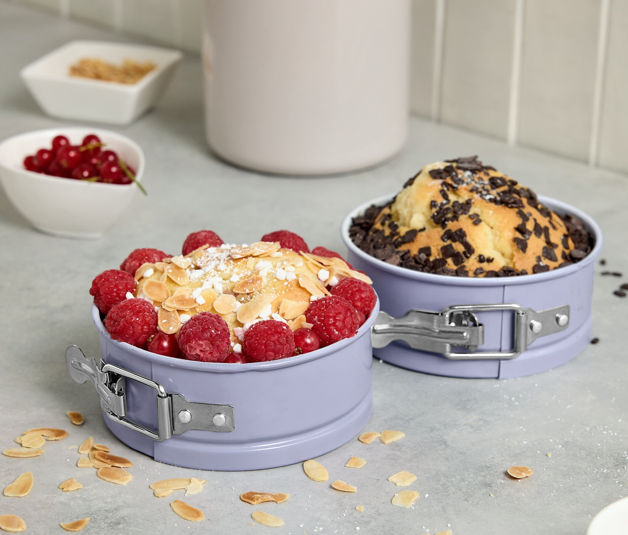 Két mini tortaforma gyümölcsökkel és csokoládéval díszített süteményekkel.