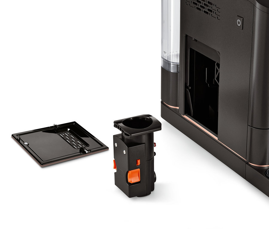 Egy fekete főzőegység a Tchibo automata kávéfőzőkhöz egy kávéfőző mellett.